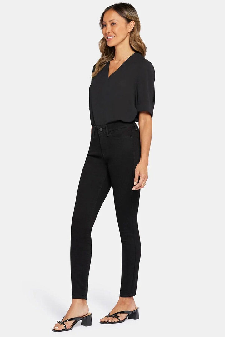Femme portant un jean skinny noir et un haut noir, style décontracté et contemporain.