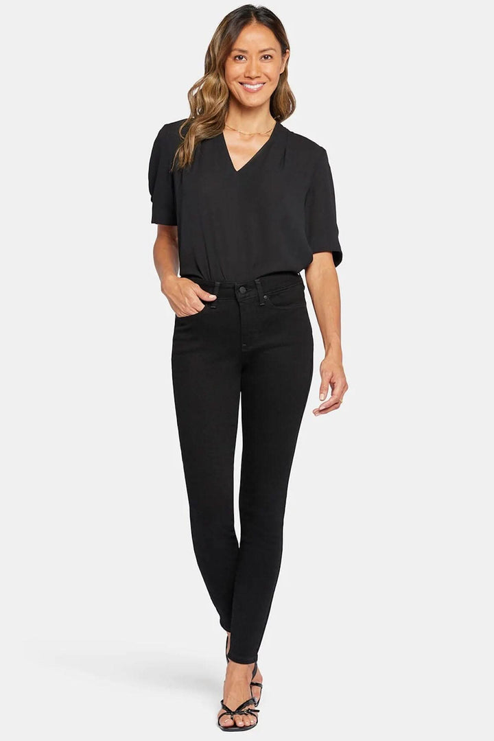 Jean skinny noir avec haut noir, modèle souriant, style chic et confortable, coupe seconde peau.