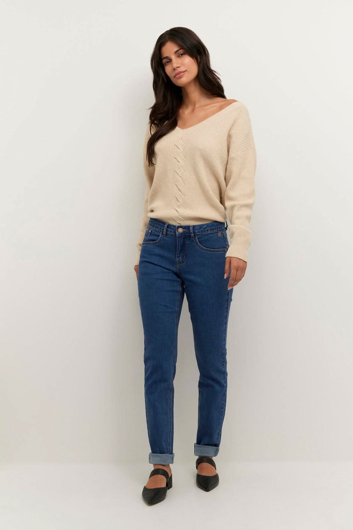 Femme portant un pull beige et un jean bleu, idéal pour toutes occasions et assorti à divers hauts.