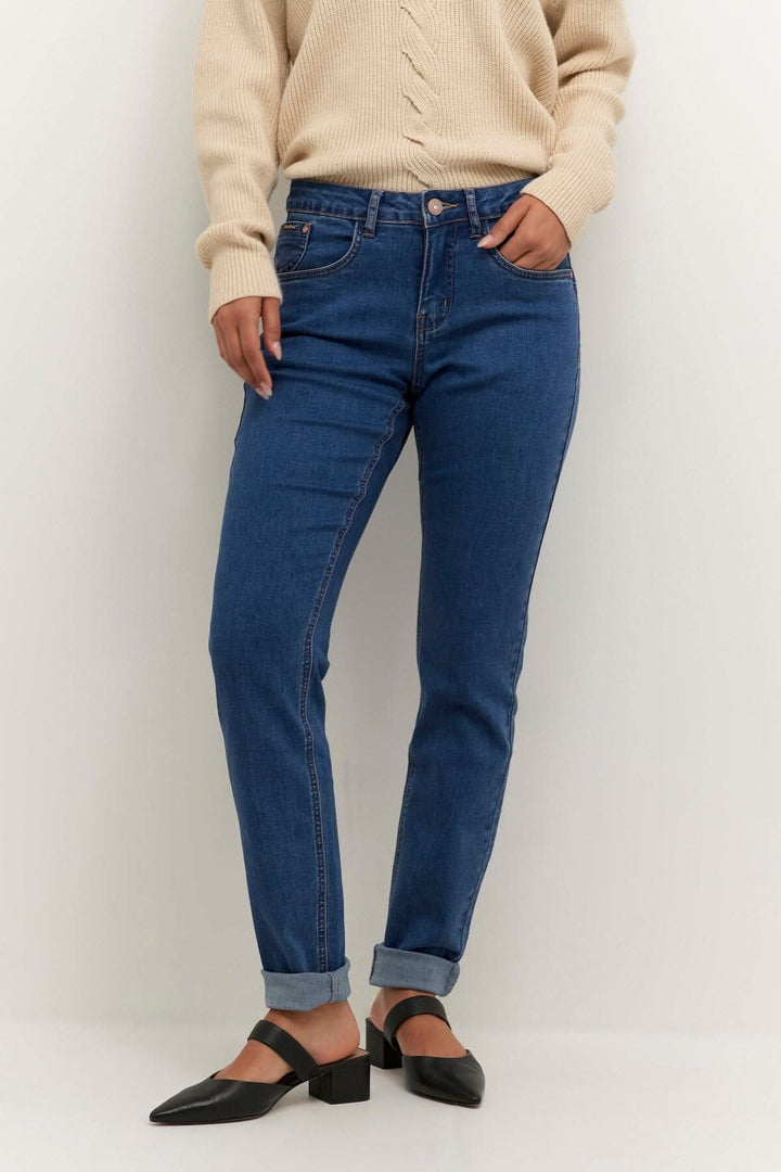 Femme portant des jeans bleus avec un pull beige, look décontracté et élégant.