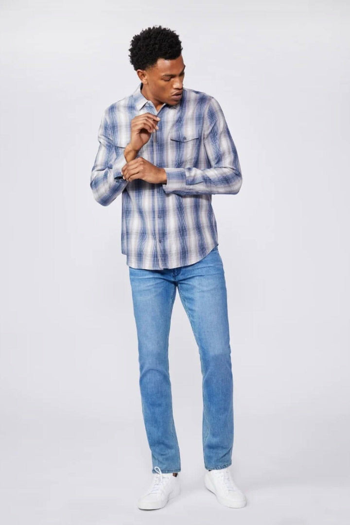Homme portant une chemise à carreaux et un jean bleu délavé, style décontracté.