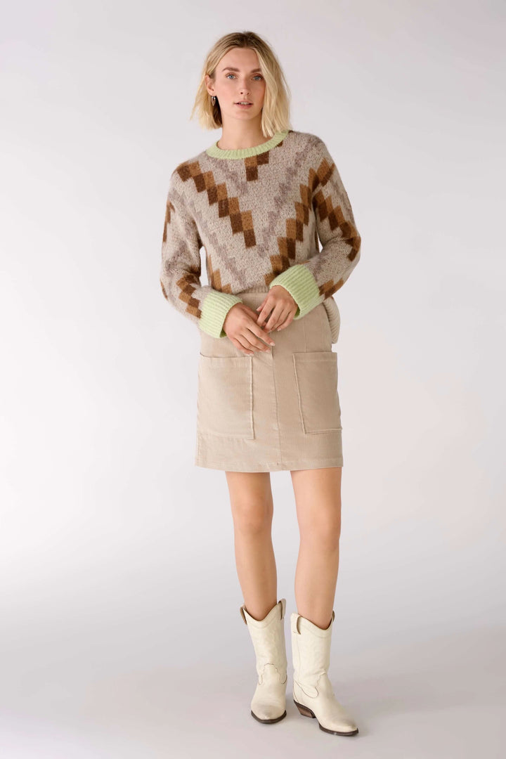 Femme portant une jupe en velours côtelé beige avec un pull graphique, chaussures blanches et un style tendance.