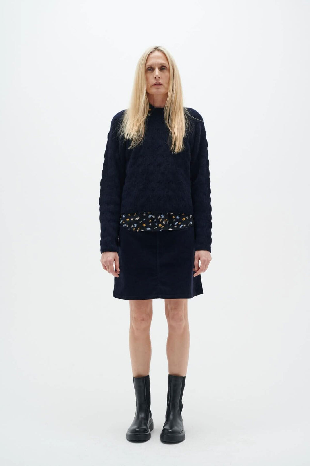 Femme en jupe marine Rylie de Inwear, avec un haut noir, bottes noires, devant un fond blanc.