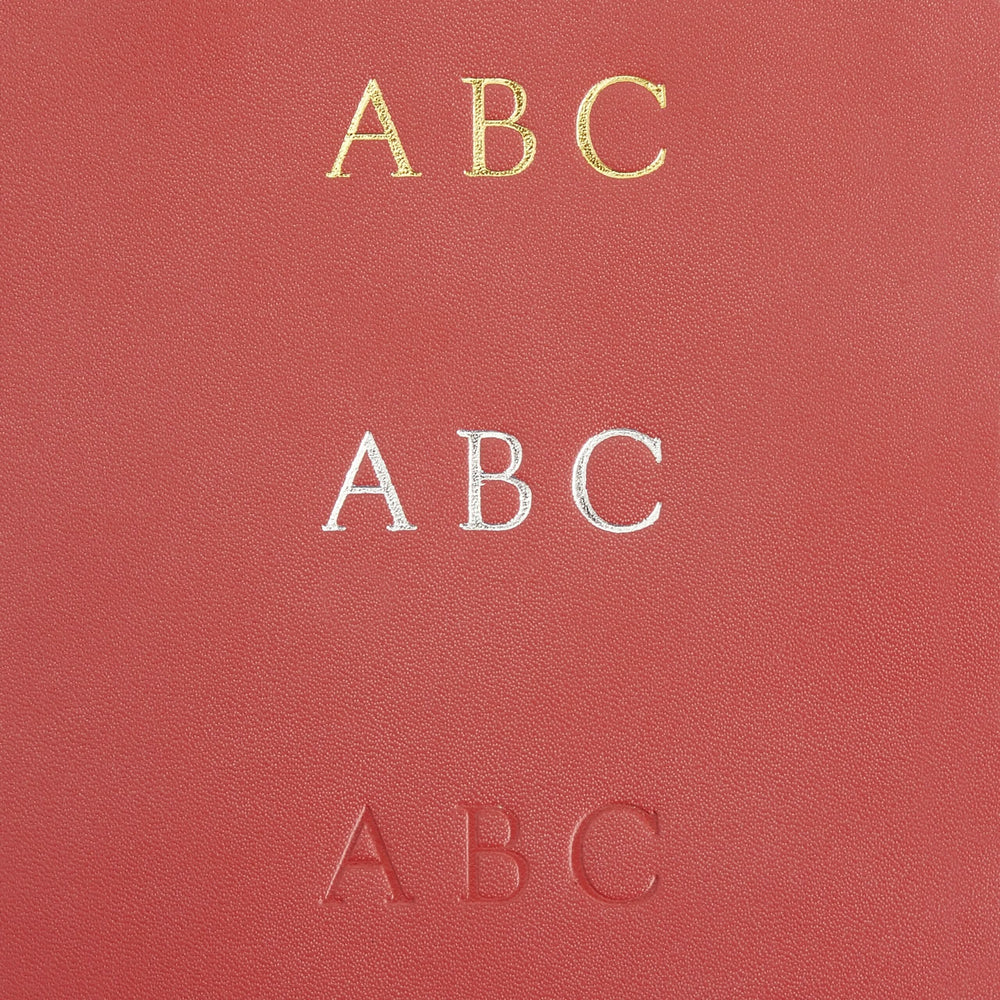 Close-up of a leather surface featuring three monogram styles: gold, silver, and embossed letters 'ABC' for personalized bookmarks.