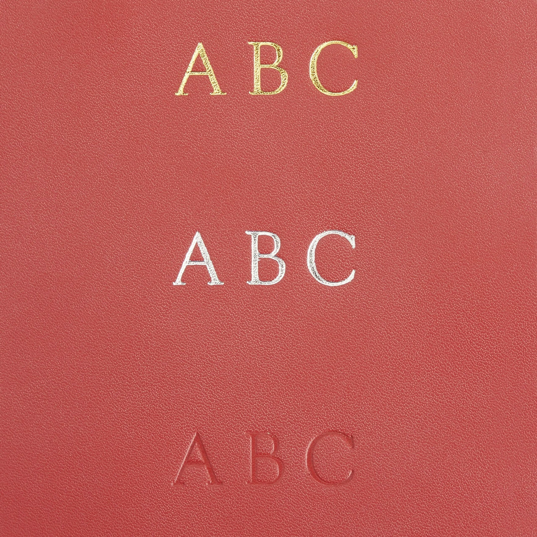 Close-up of a leather surface featuring three monogram styles: gold, silver, and embossed letters 'ABC' for personalized bookmarks.