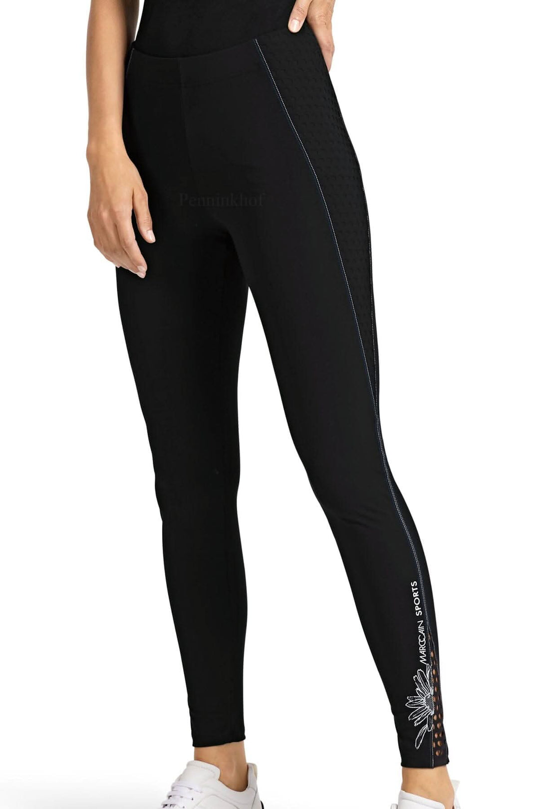Legging de sport noir Marc Cain avec couture blanche et bleue, motif marguerite sur le mollet gauche.