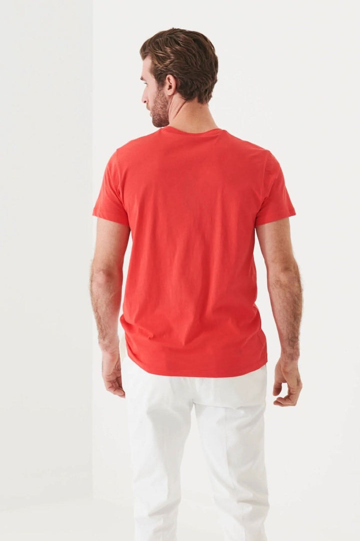 Homme portant un t-shirt léger en coton pima rouge, vu de dos, avec pantalon blanc, dans un environnement lumineux.
