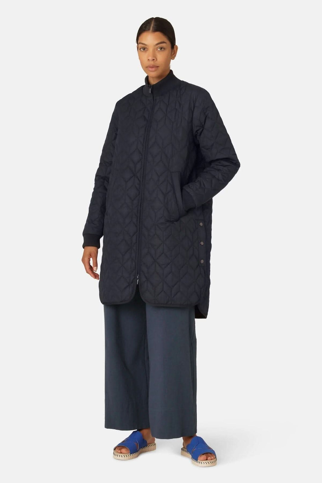 Manteau matelassé long en bleu marine avec poches et fermeture à glissière, porté par une femme.