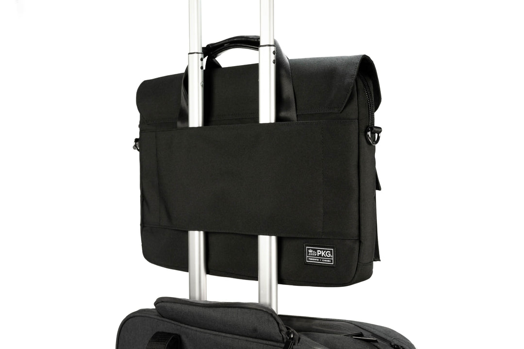 Sac Messager PKG Richmond 10L noir, avec rabat magnétique, sur une valise trolley de voyage.