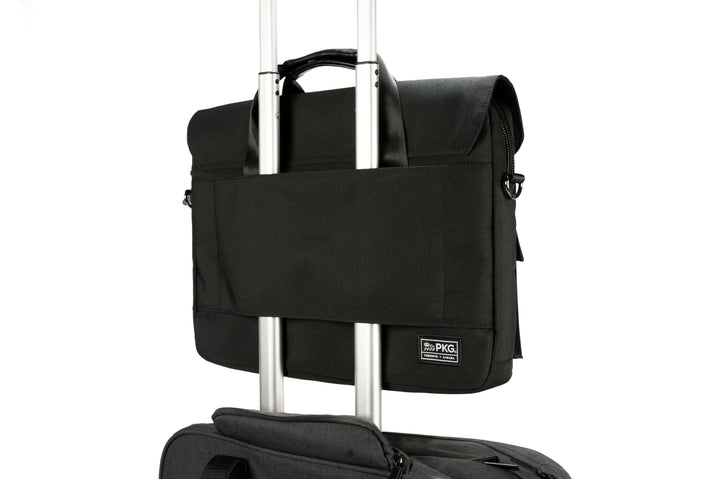 Sac Messager PKG Richmond 10L noir, avec rabat magnétique, sur une valise trolley de voyage.