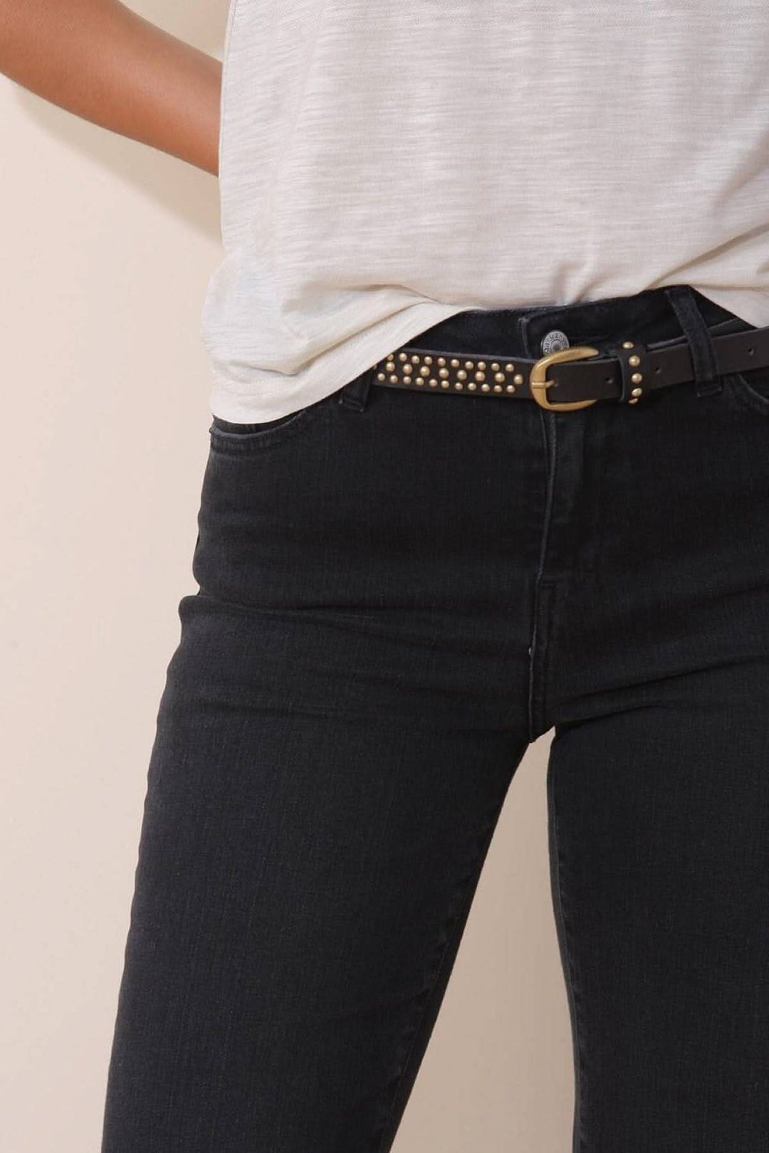 Mini ceinture à clous dorés en cuir portée avec un t-shirt et un jean noir, ajoutant une touche originale.