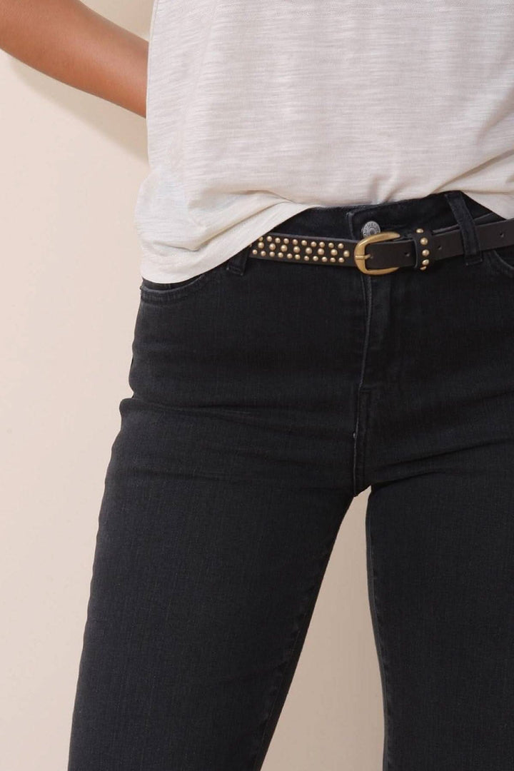 Mini ceinture à clous dorés en cuir portée avec un t-shirt et un jean noir, ajoutant une touche originale.