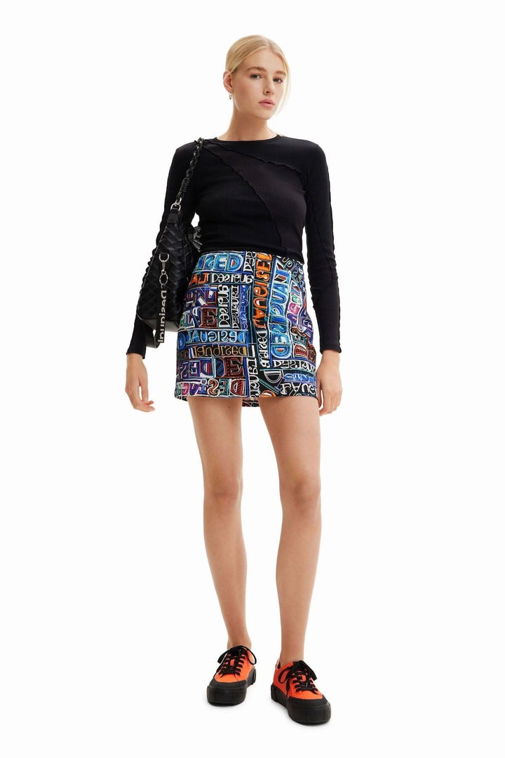 Mini-jupe slim haute avec imprimé logo arty coloré, portée avec un haut noir et des baskets orange.