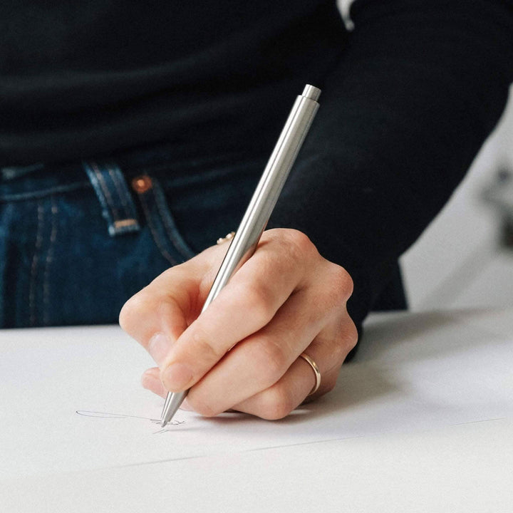 Main d'une personne tenant un stylo moderne en train d'écrire sur du papier avec un fond flou.