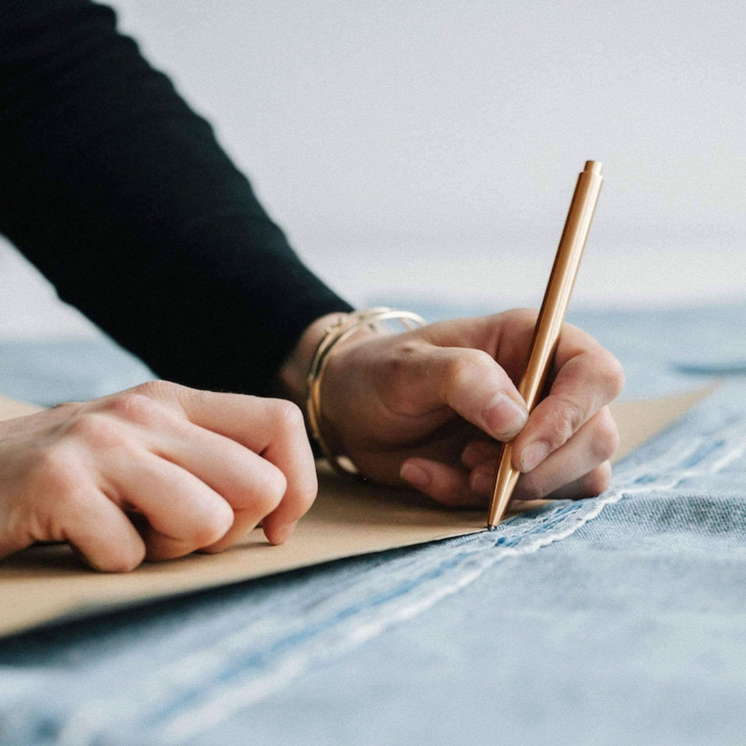 Une main tenant un stylo doré trace des lignes sur du denim, illustrant un processus créatif.