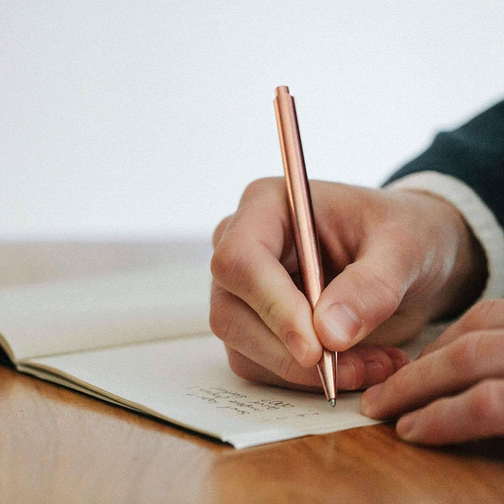 Stylos modernes en rose doré, main écrivant dans un carnet, parfaite pour des notes élégantes.