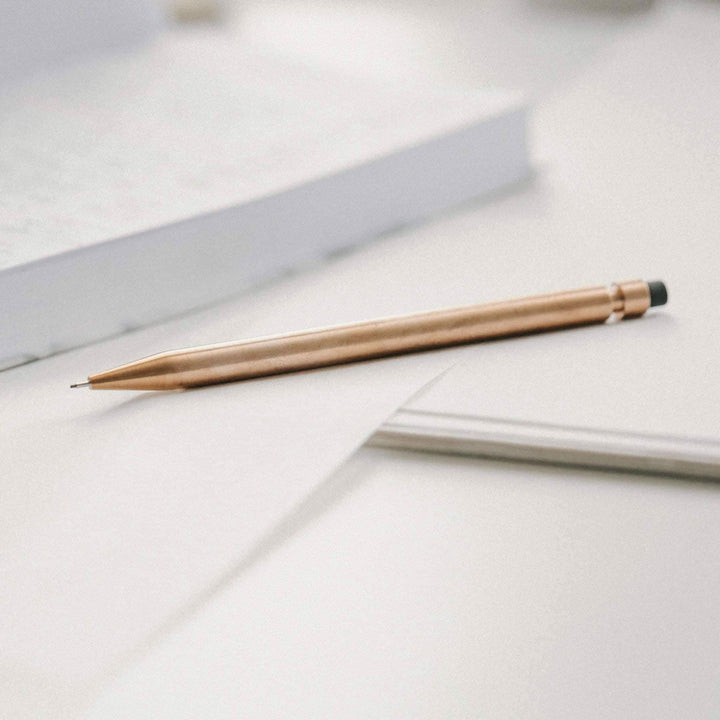 Crayon Modern Fuel en métal solide, design unique sans plastique, posé sur du papier avec livres en arrière-plan.