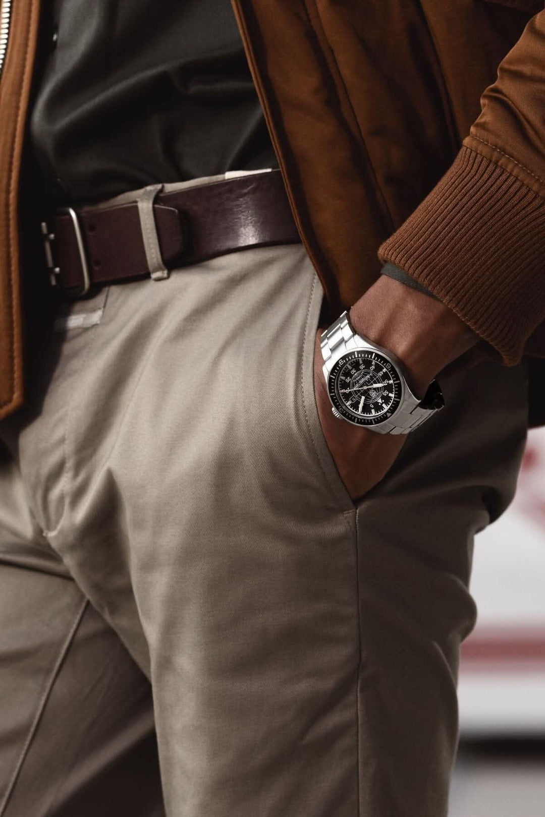 Montre élégante portée au poignet avec pantalon beige et ceinture marron, mettant en valeur un style moderne.