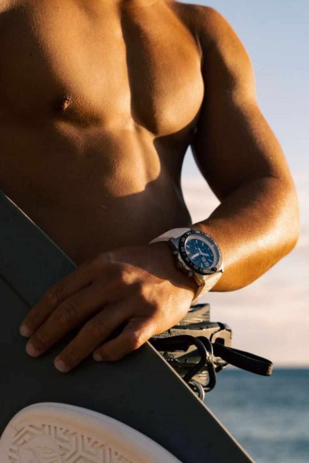 Homme en maillot de bain tenant une planche de surf avec une montre Luminox Pacific Diver 3141 au poignet.