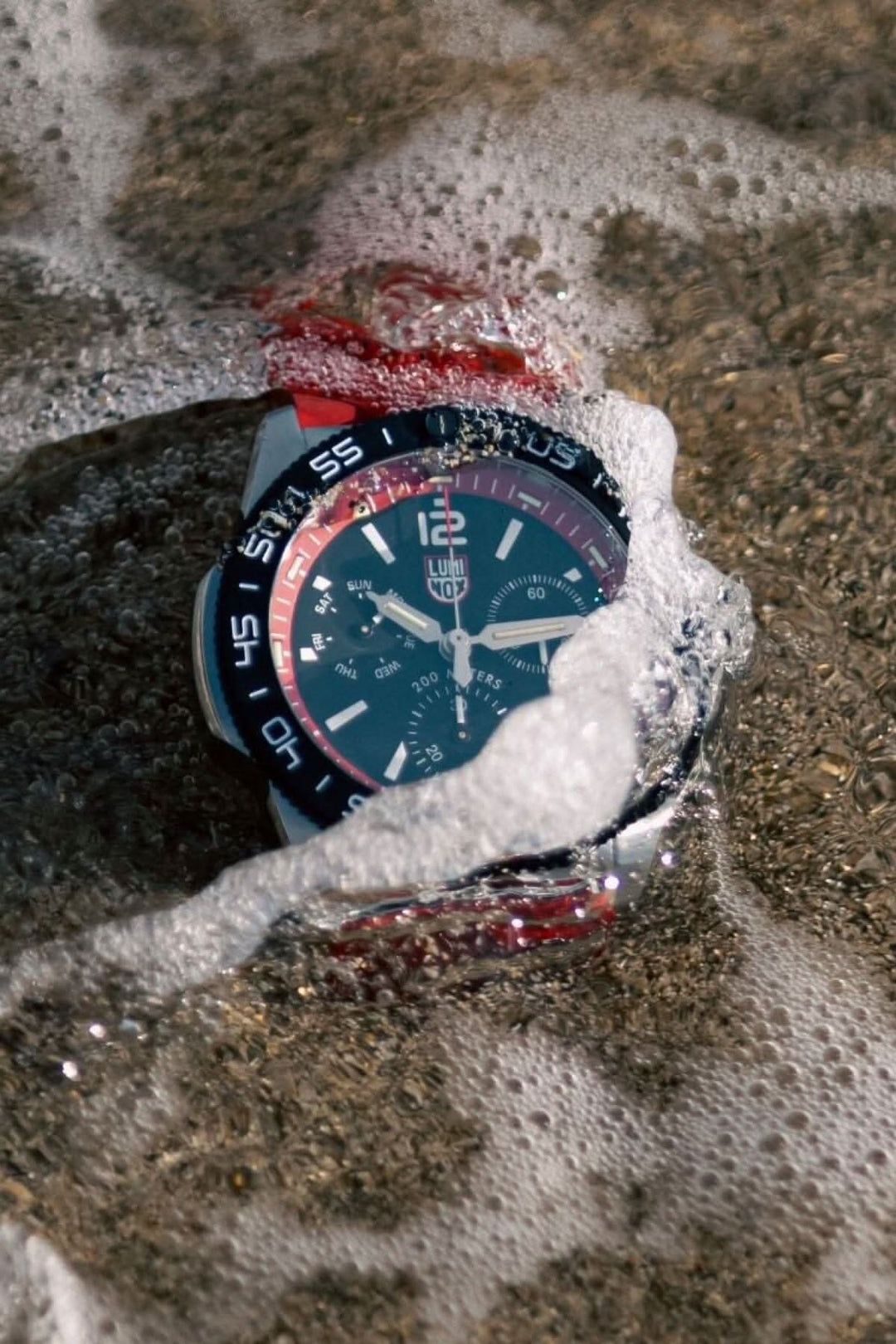 Montre Luminox Pacific Diver 3155 submergée dans l'eau, sur le sable, avec des vagues qui l'entourent.