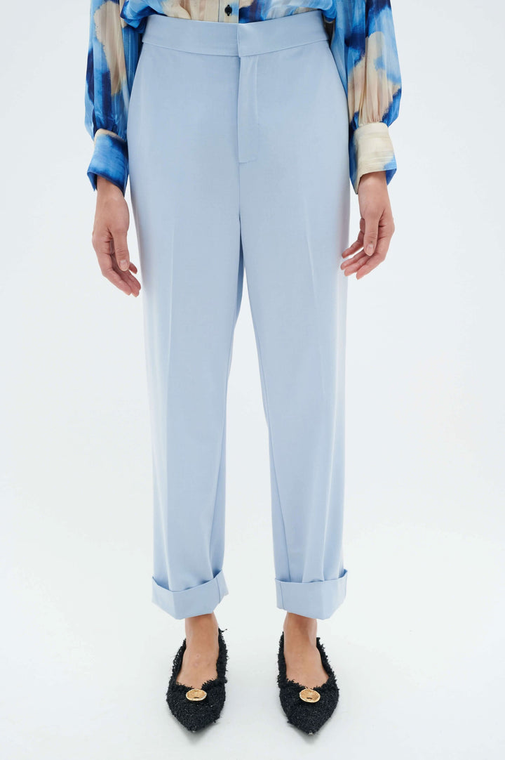 Pantalon à revers Naxa, jambe fuseau, taille élastique, poches, couleur bleue, porté avec des chaussures élégantes.