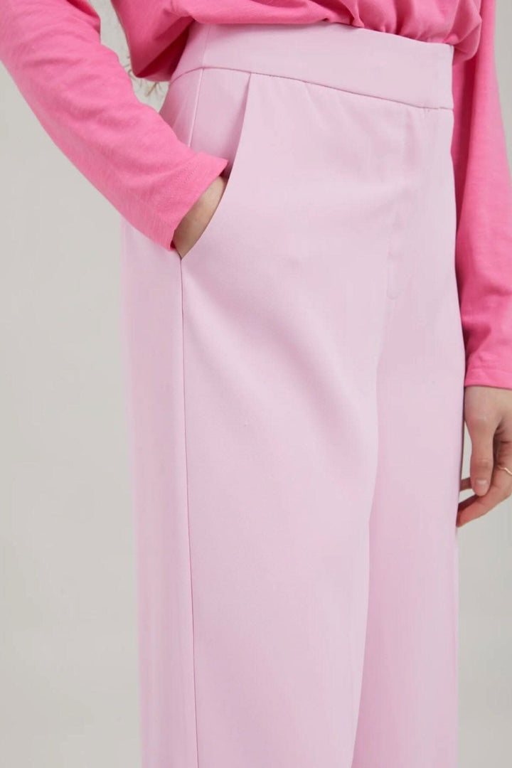 Pantalon Alba en rose avec jambes larges, poches et fermeture à glissière, porté avec un haut rose.