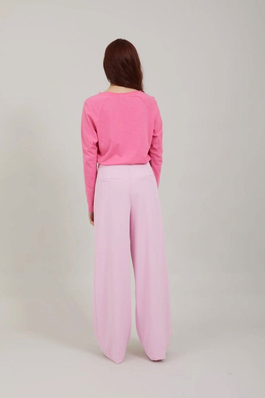 Femme de dos portant un pull rose et un pantalon large rose, style décontracté et chic.