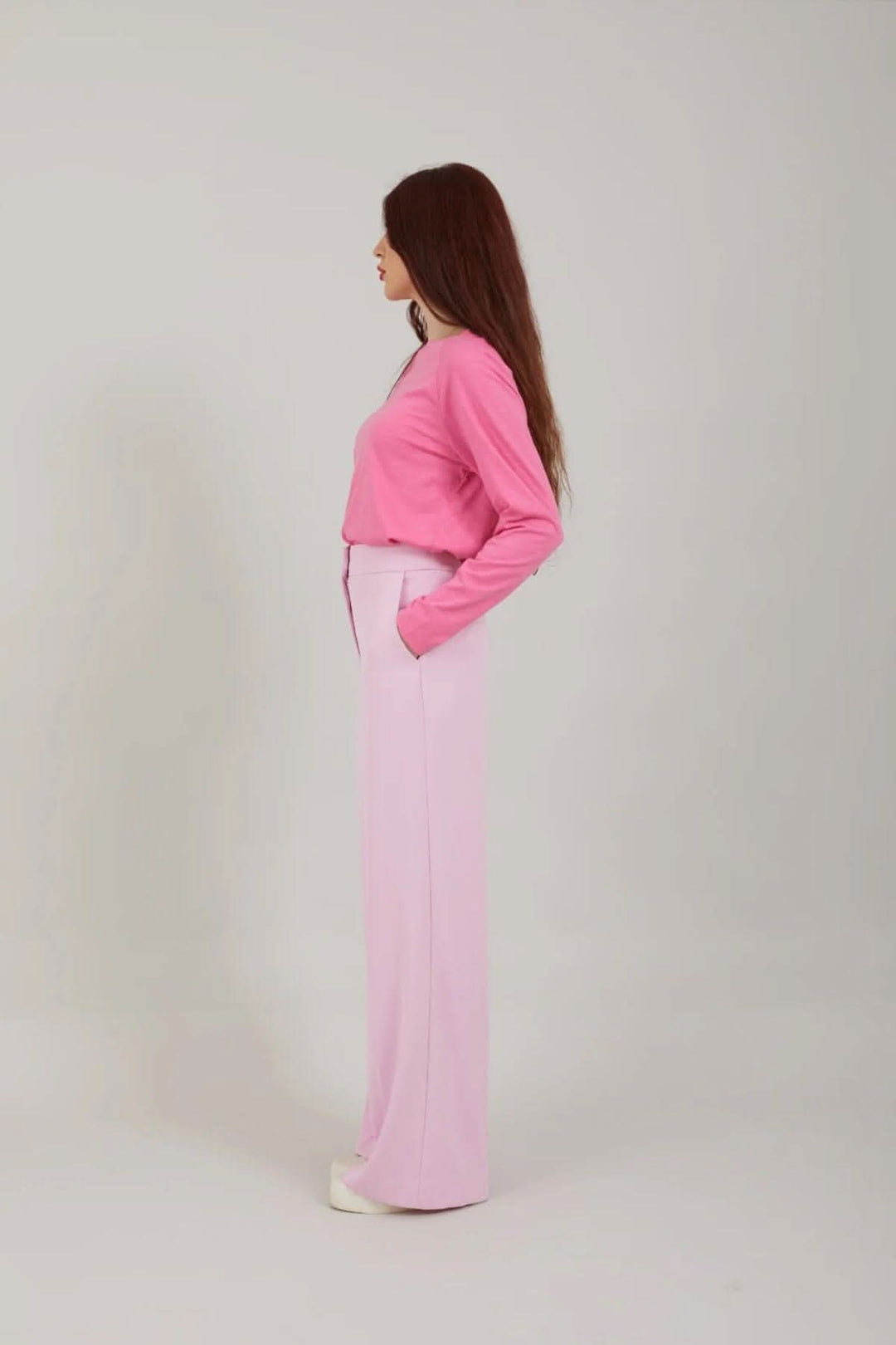 Femme portant un pantalon larga coloré avec une chemise rose, pose de côté sur fond neutre.
