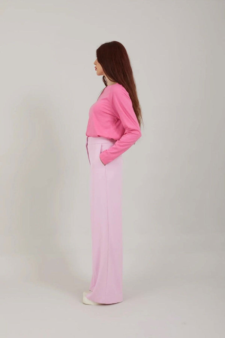 Femme portant un pantalon larga coloré avec une chemise rose, pose de côté sur fond neutre.