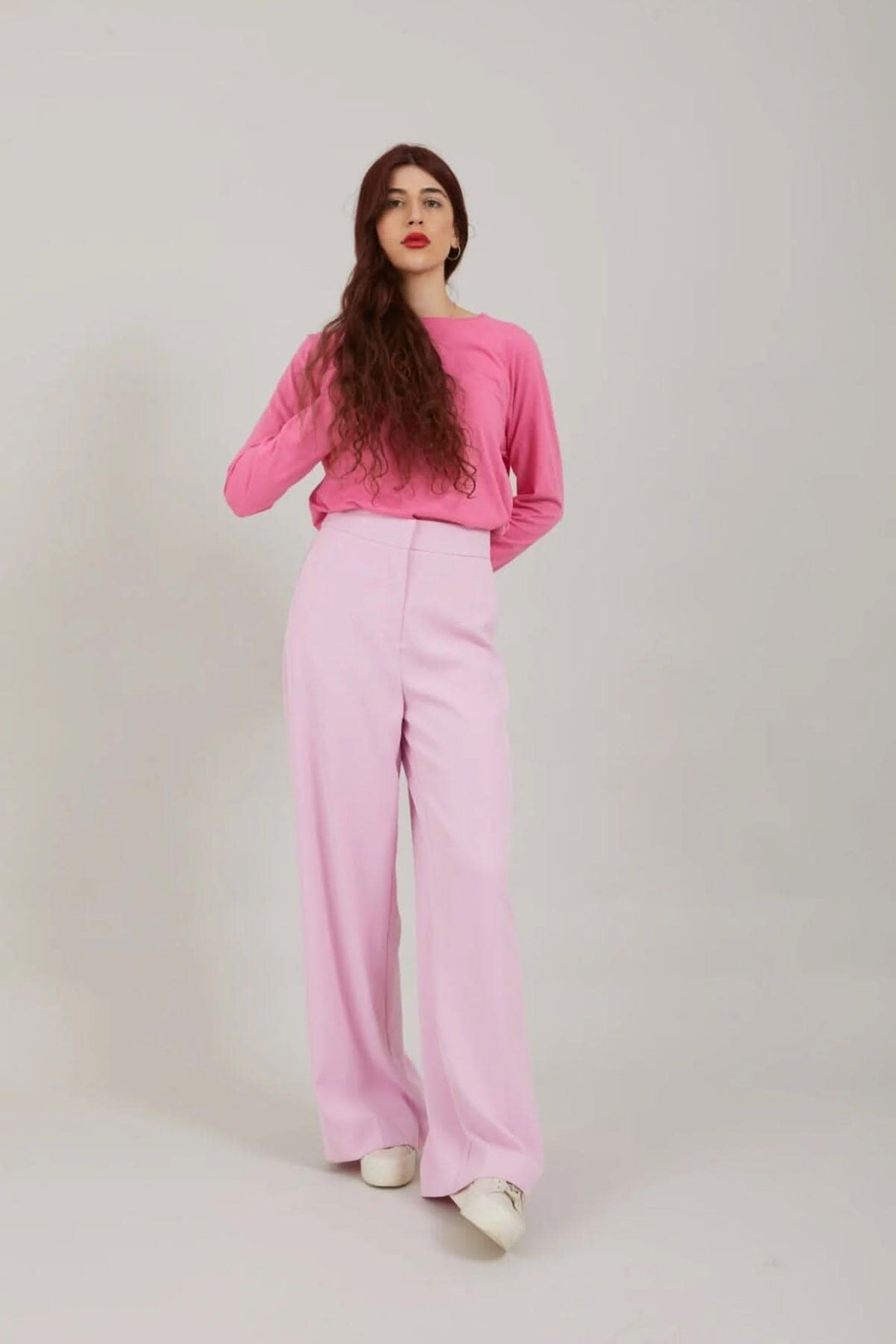 Femme portant un pantalon large rose avec un haut rose, se tenant debout sur fond neutre.