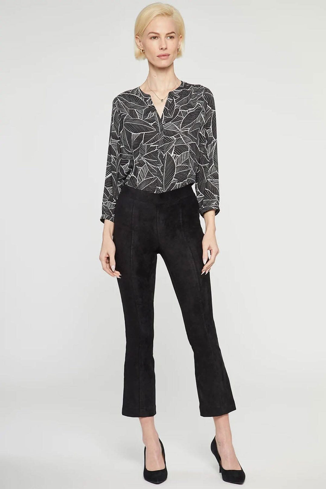 Femme portant un pantalon bootcut mince en faux daim et une blouse à motif feuillage.
