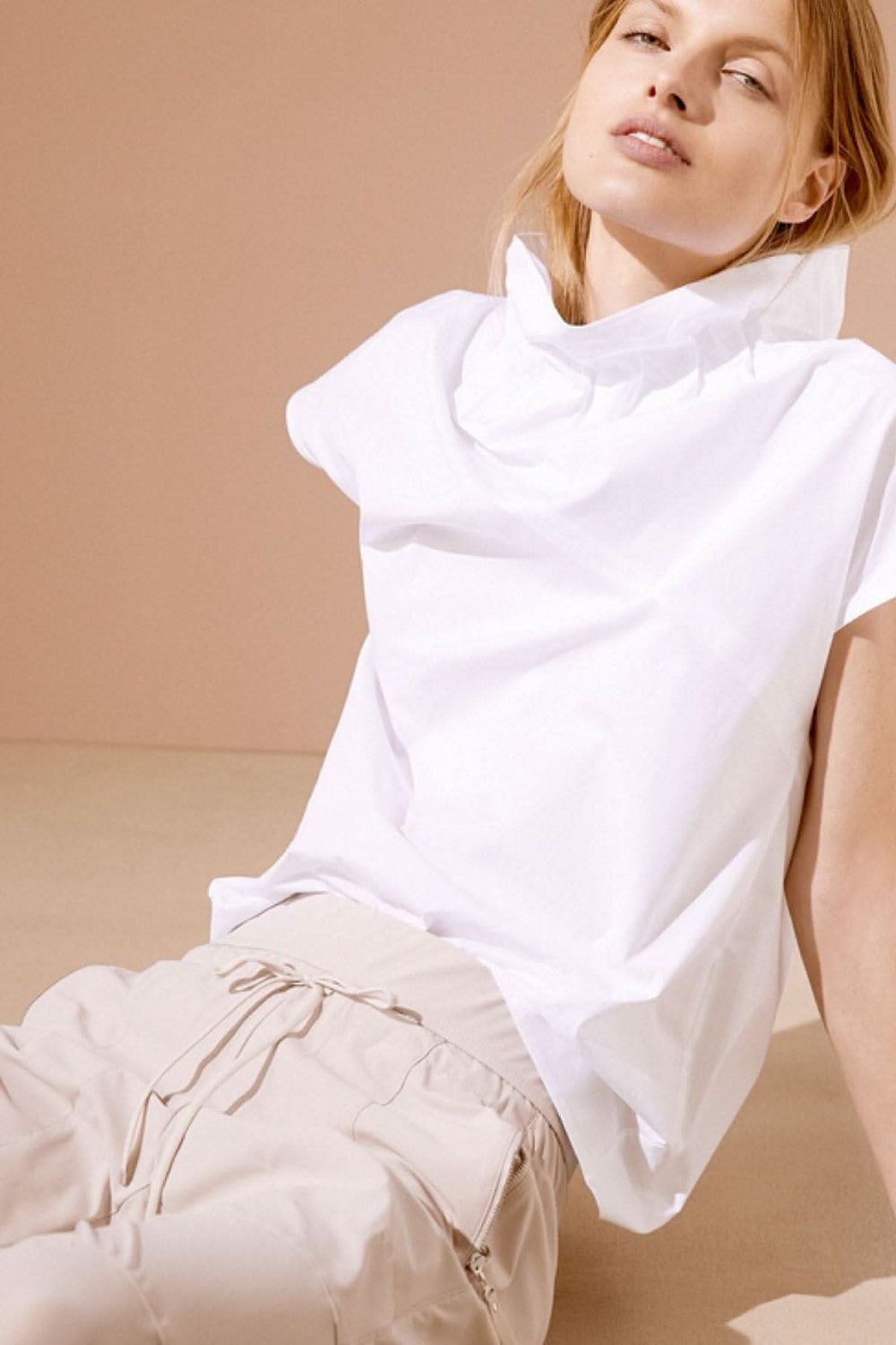 Modèle féminin portant un haut blanc élégant avec pantalon décontracté, style moderne sur fond rose.