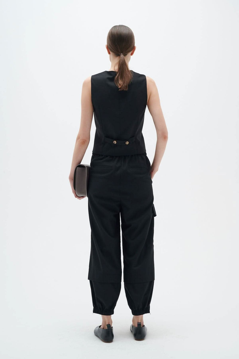 Femme vêtue d'un pantalon cargo noir, vue de dos, avec un haut sans manches et une pochette.