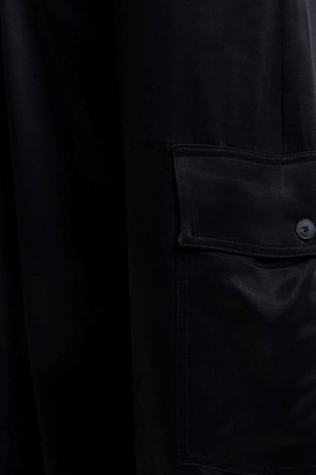 Détail d'un pantalon cargo large en satin noir avec poche latérale à bouton.