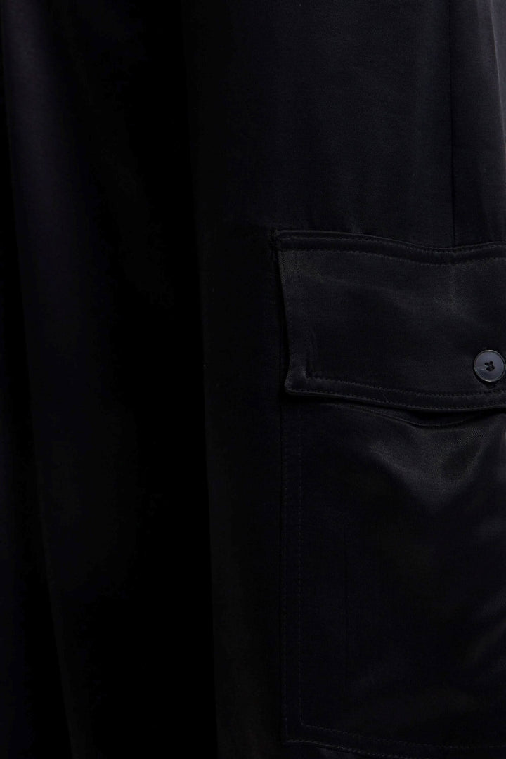 Détail d'un pantalon cargo large en satin noir avec poche latérale à bouton.
