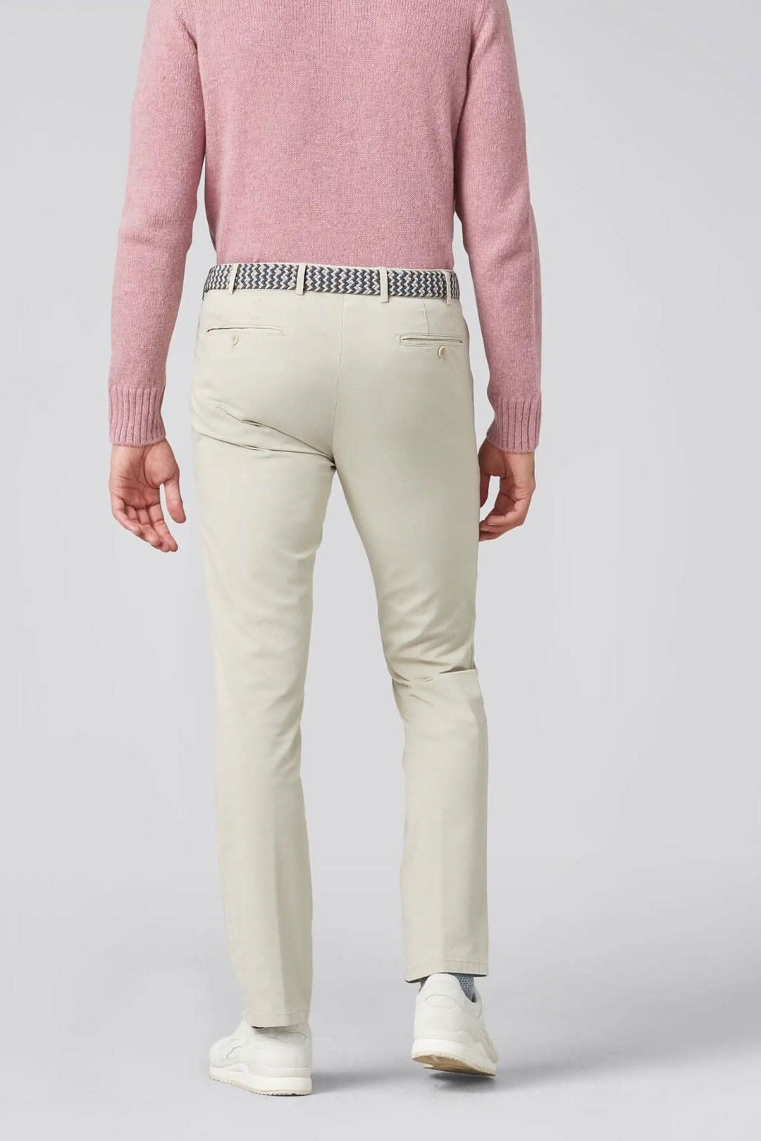 Pantalon chino beige porté par un homme de dos, avec un pull rose et ceinture à motif.