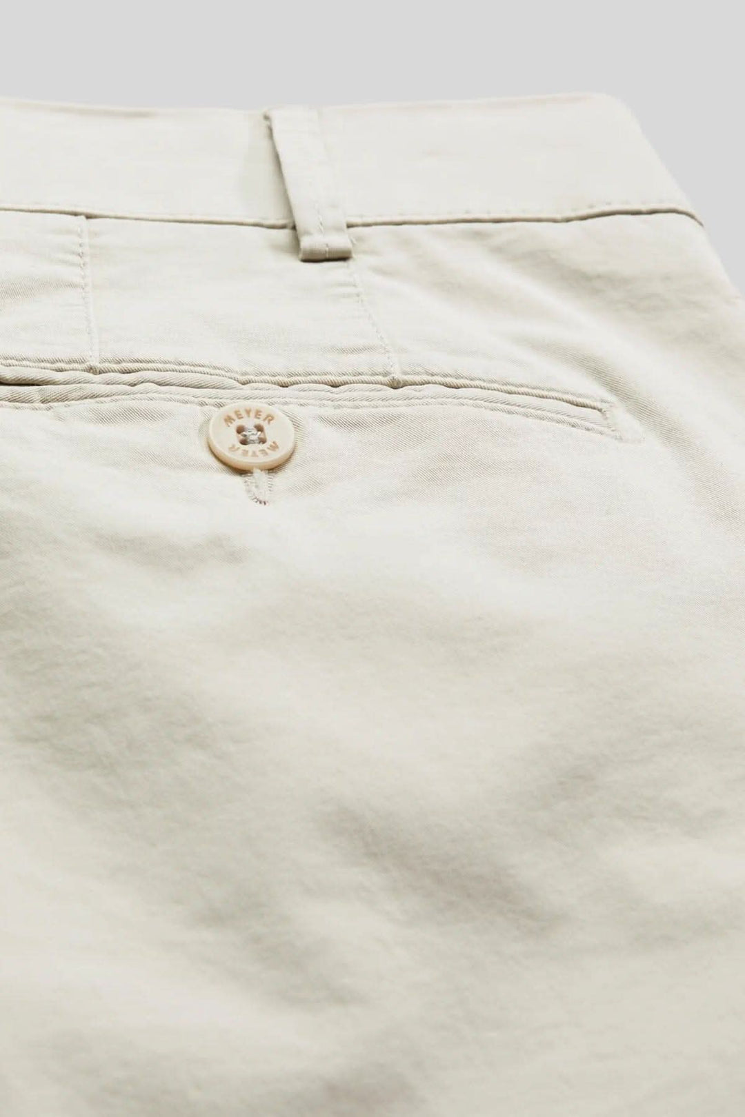 Détail d'un pantalon chino beige avec bouton et couture arrière, alliant confort et style tendance.