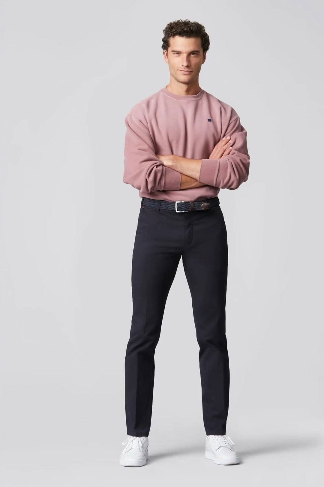 Homme portant un pantalon chino noir et un sweat rose, posant avec confiance.