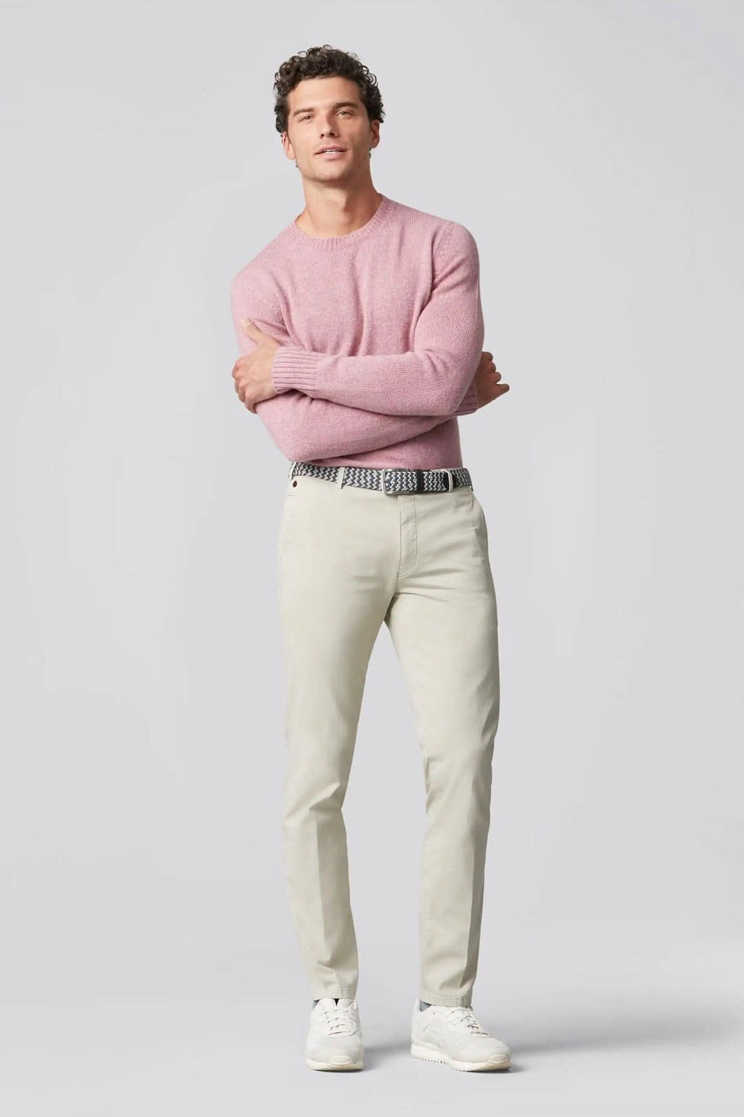 Homme portant un pantalon chino beige et un pull rose, affichant une tenue moderne et élégante.