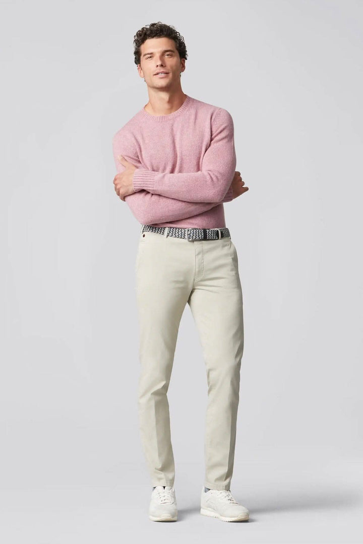 Homme portant un pantalon chino beige et un pull rose, affichant une tenue moderne et élégante.