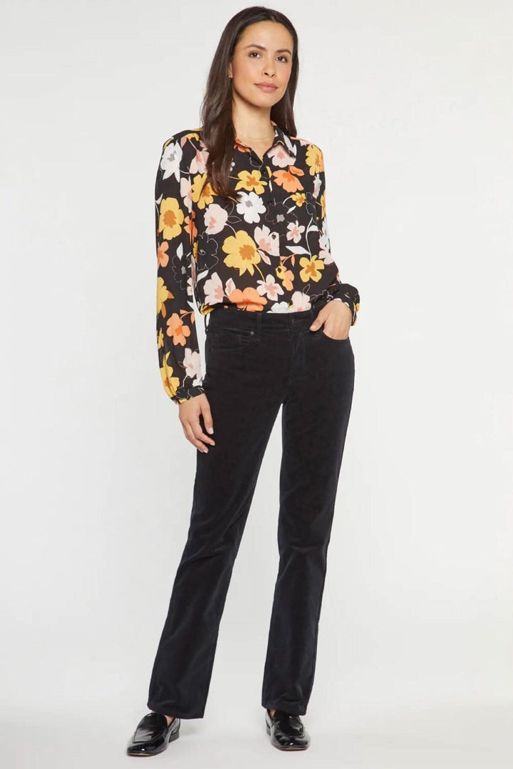 Femme en pantalon droit Marilyn en velours côtelé, associée à une blouse à fleurs élégante.