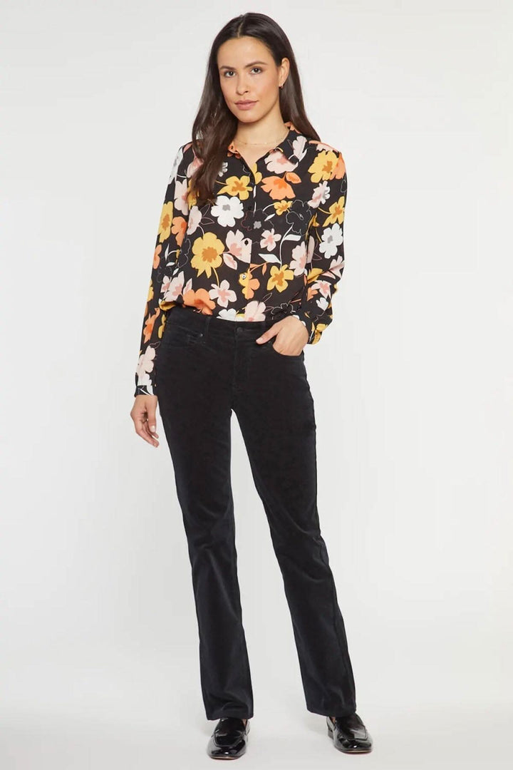 Femme portant un pantalon droit en velours côtelé noir, associé à une blouse florale colorée.