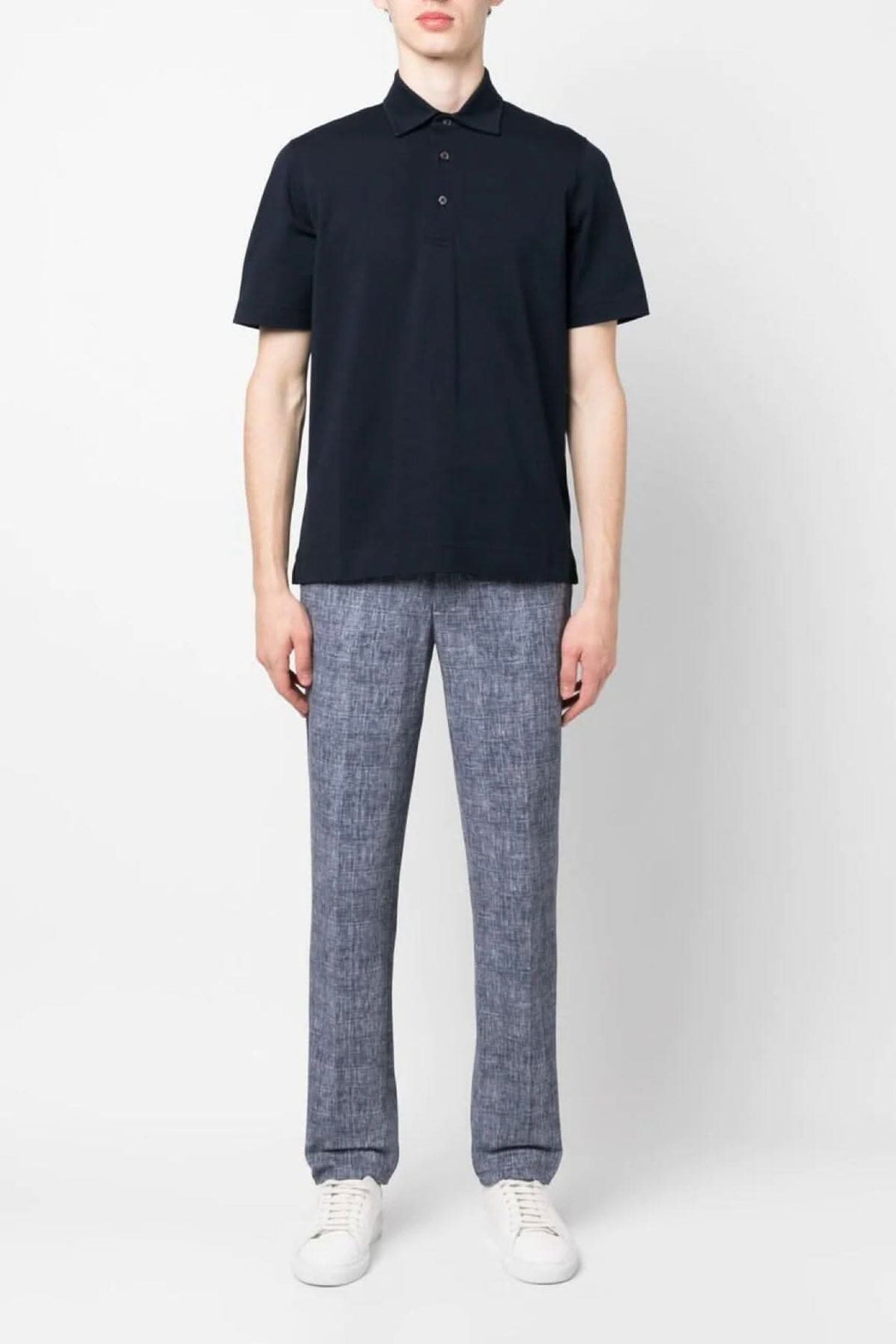 Homme portant un polo noir et un pantalon bleu à carreaux, avec des chaussures blanches.