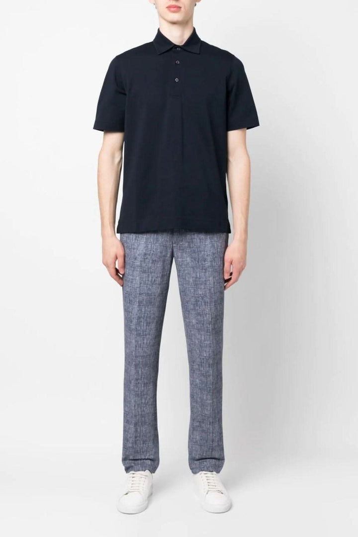 Homme portant un polo noir et un pantalon bleu à carreaux, avec des chaussures blanches.