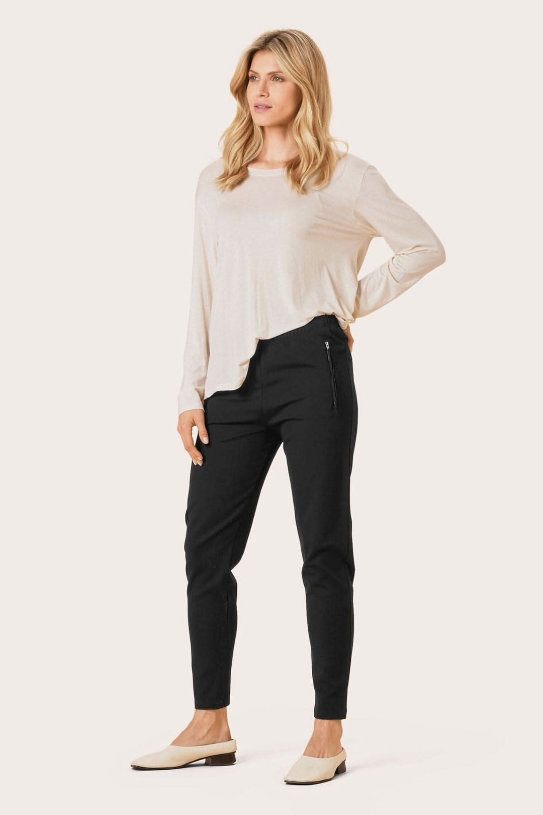 Femme portant un pantalon en jersey noir et un haut beige, avec poches zippées pour un look décontracté et élégant.