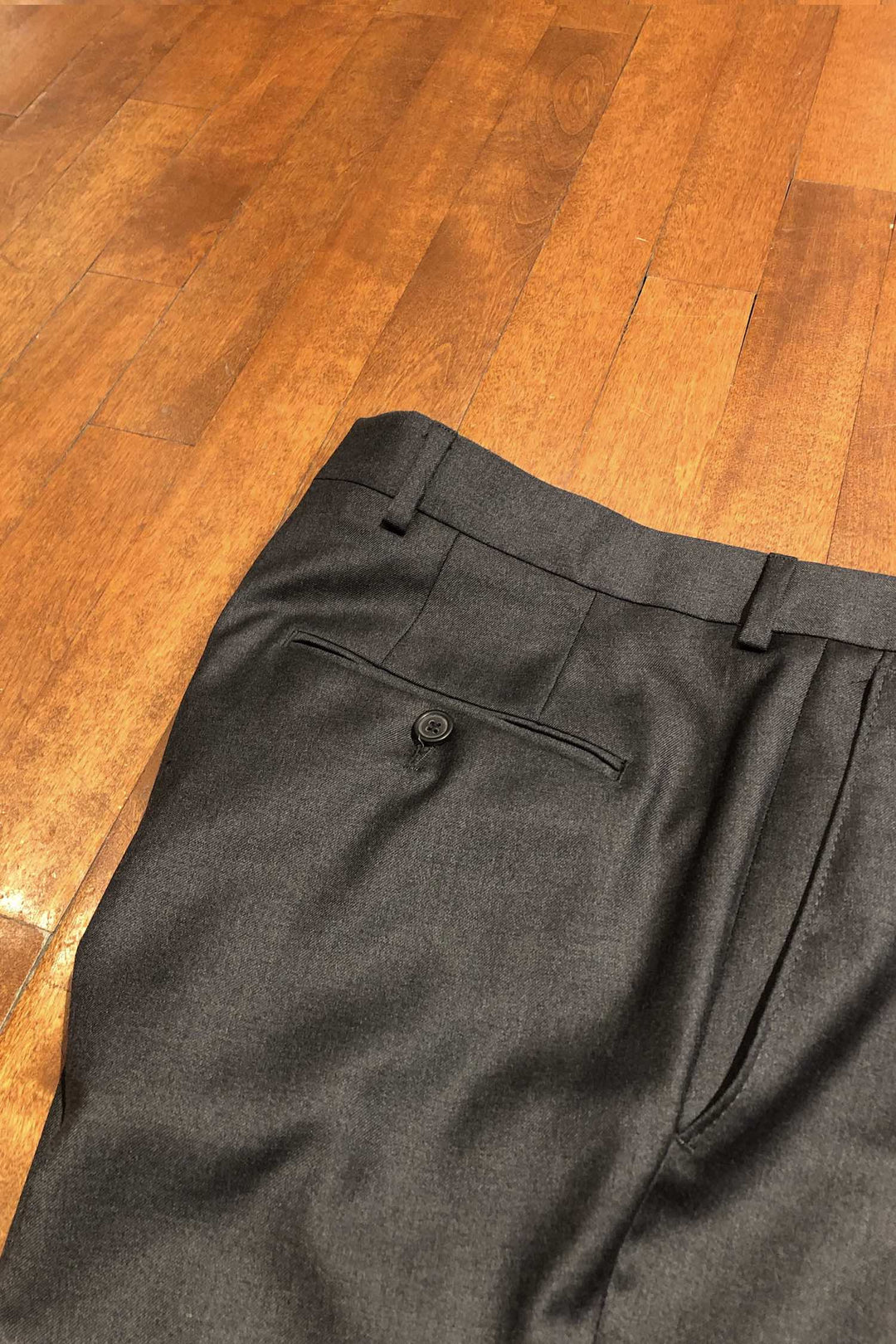Pantalon en laine Samuelsohn noir, détail de la poche arrière sur un sol en bois.