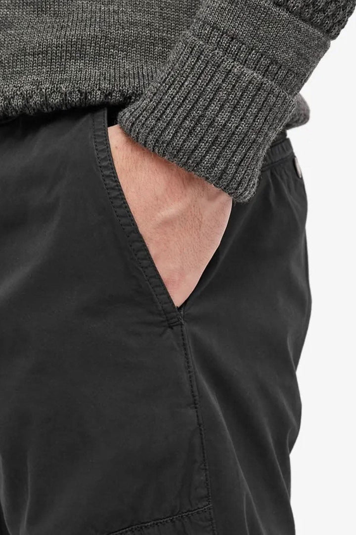 Détail d'un pantalon noir en twill stretch avec une main dans la poche, combiné avec un pull gris.