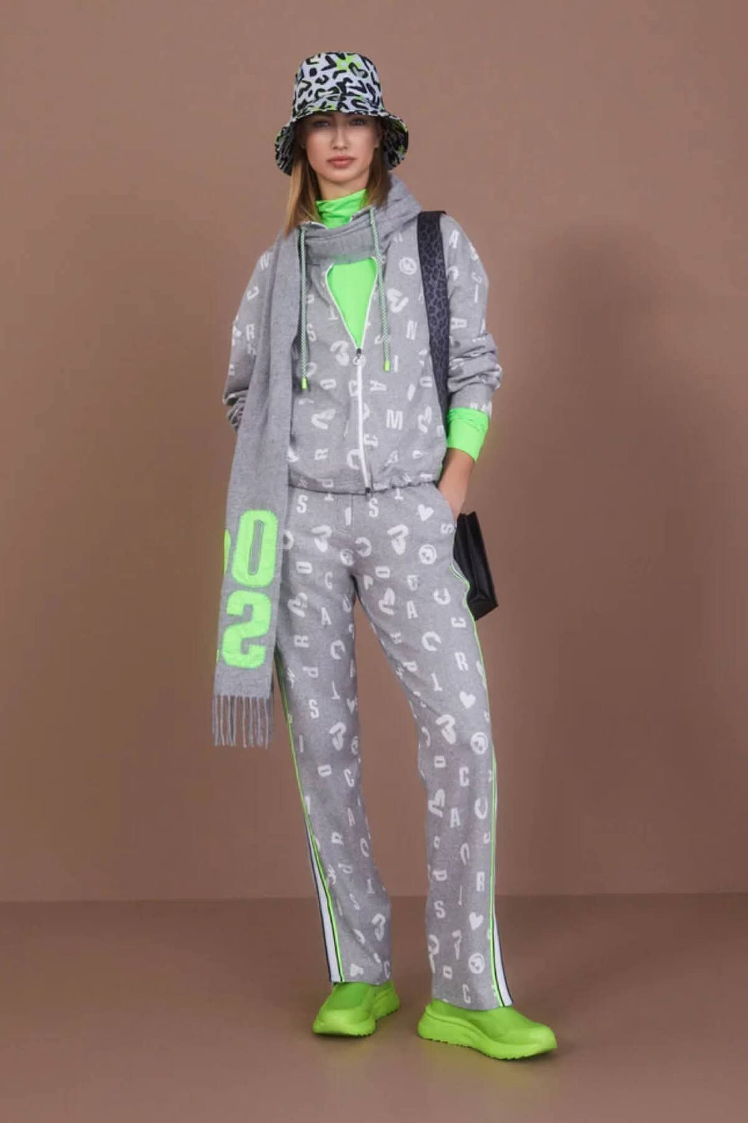 Modèle portant un ensemble jogging gris avec motifs, accessoires verts fluo et chapeau à motifs.