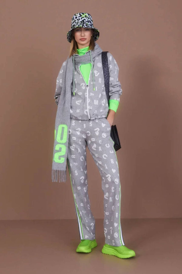 Modèle portant un ensemble jogging gris avec motifs, accessoires verts fluo et chapeau à motifs.