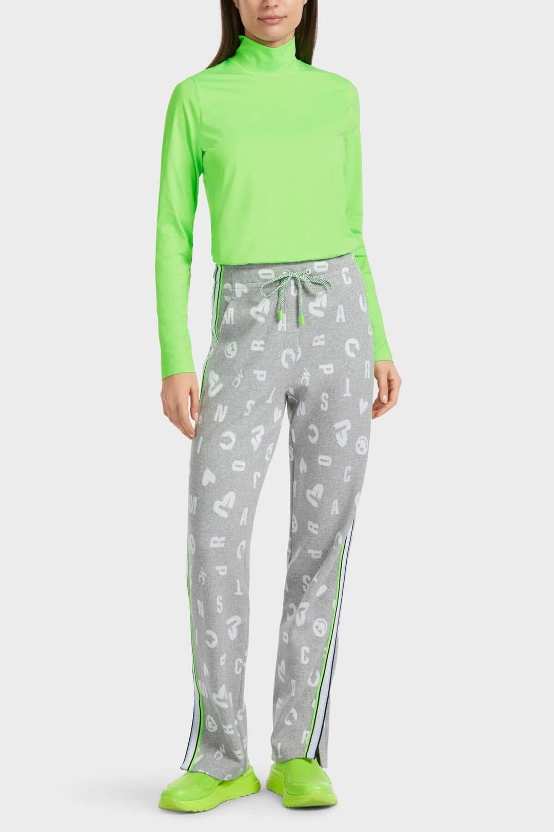 Pantalon jogging gris argenté avec motifs lettres et cœurs, porté avec un haut vert fluo.